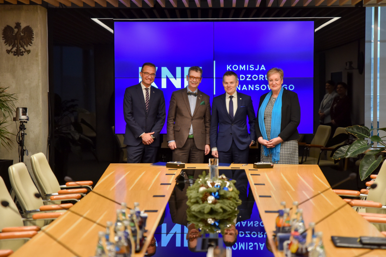 trzech mężczyzn i kobieta w sali konferencyjnej po podpisaniu porozumienia