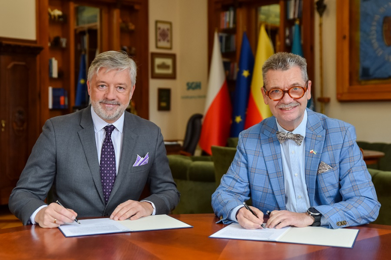 dwóch mężczyzn siedzi przy biurku po podpisaniu umowy