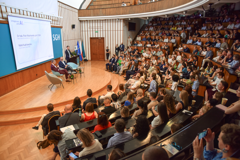 aula uczelniana wypełniona tłumem gości, na scenie rozmawia dwóch mężczyzn