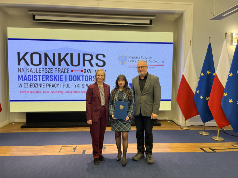 dwie kobiety i mężczyzna pozują do zdjęcia na tle ekranu i czterech flag: RP i UE ustawionych naprzemiennie