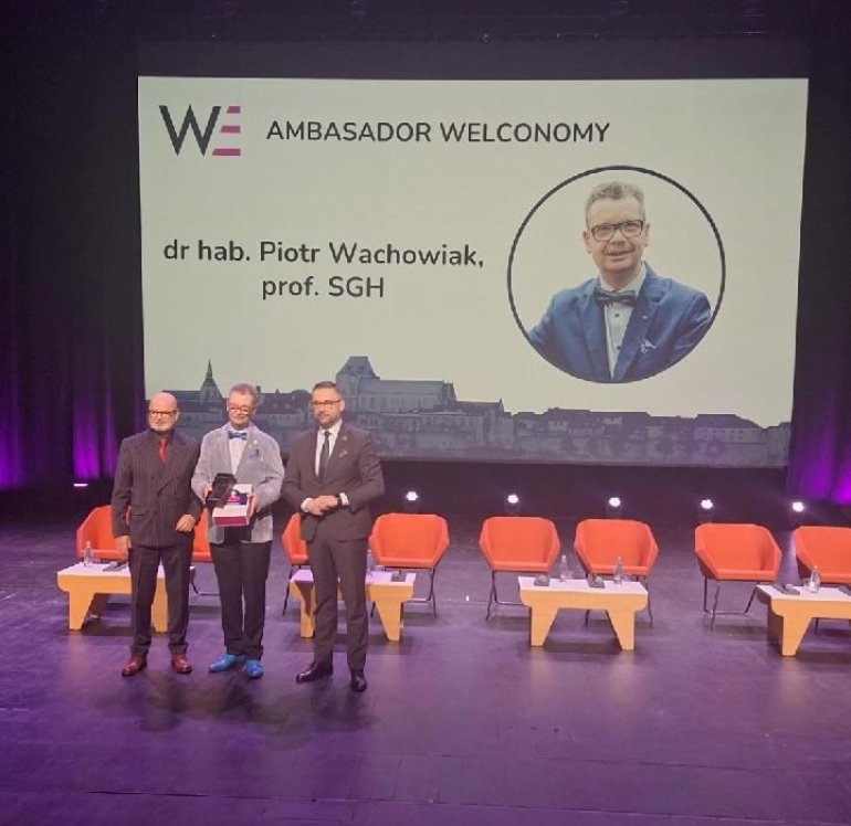 trzech mężczyzn stoi na scenie, jeden odbiera nagrodę