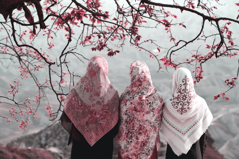 trzy kobiety muzułmańskie w chustach odwrócone tyłem; w tle kwitnące drzewo