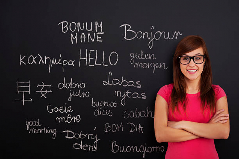 lektorka języków obcych stoi przed tablicą, na której widnieją wypisane kredą słowa w różnych językach