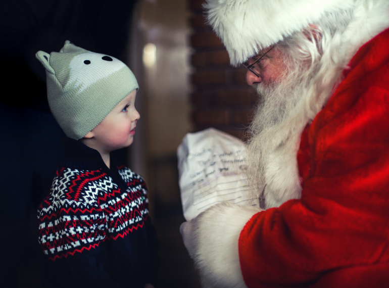 zdjęcie kolorowe. Święty Mikołaj pochylony w życzliwej rozmowie z małym chłopcem.