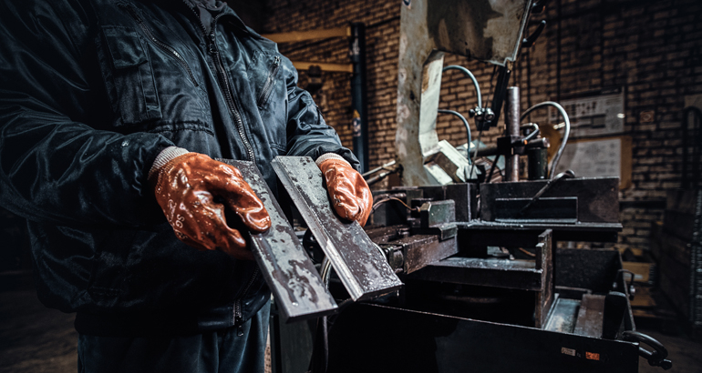 Na zdjęciu pracownik w rękawicach ochronnych trzyma świeżo ścięty kawałek metalu - autor fxquadro