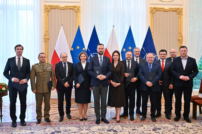 grono oficjeli pozuje do zdjęcia; w tle flagi Polski, UE, NATO